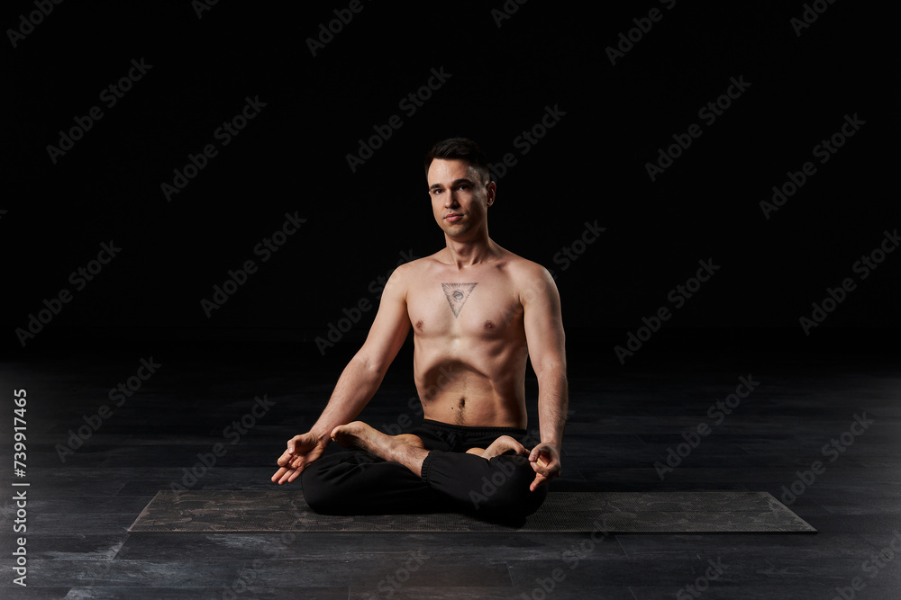 The man in lotus meditation, abdomen vacuumed, bears an all-seeing eye tattoo on his chest, symbolizing spiritual insight.