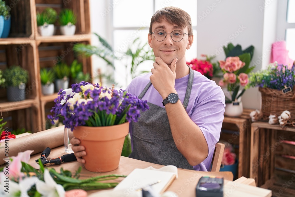 Caucasian blond man working at florist shop looking confident at the camera smiling with crossed arms and hand raised on chin. thinking positive.