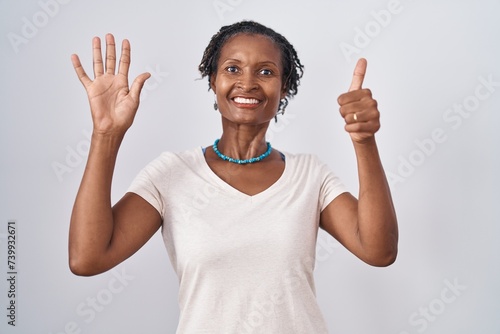 African woman with dreadlocks standing over white background showing and pointing up with fingers number six while smiling confident and happy.