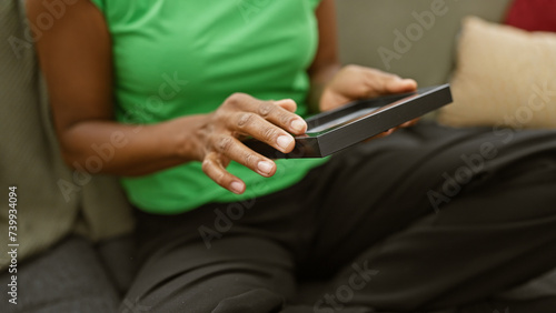 Black woman holding a photo frame while seated on a sofa indoors, suggesting a moment of nostalgia or reflection.
