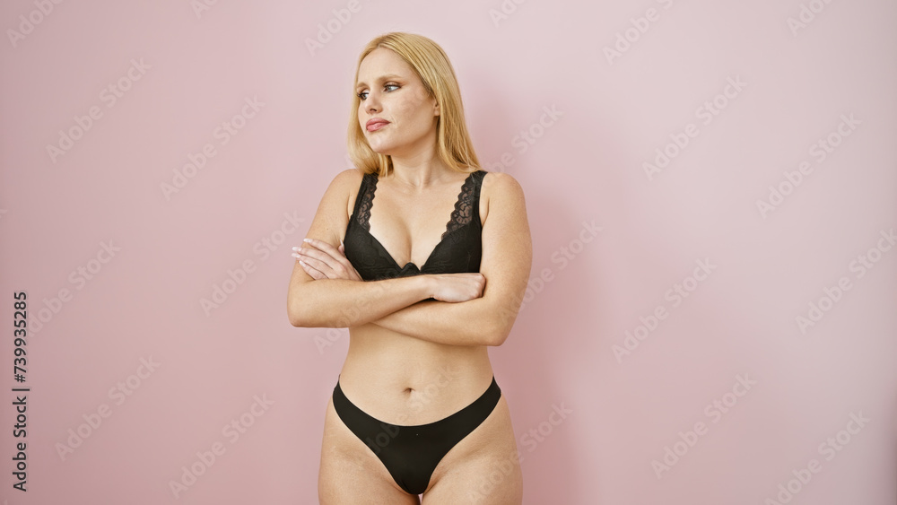 Confident blonde woman in lingerie poses against a pink background, exuding body positivity. Confident blonde woman in lingerie poses against a pink background, exuding body positivity.