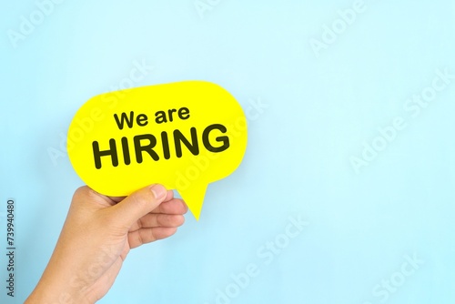 Human hand holding yellow speech bubble with written phrase We are Hiring. Recruitment and job hiring concept.