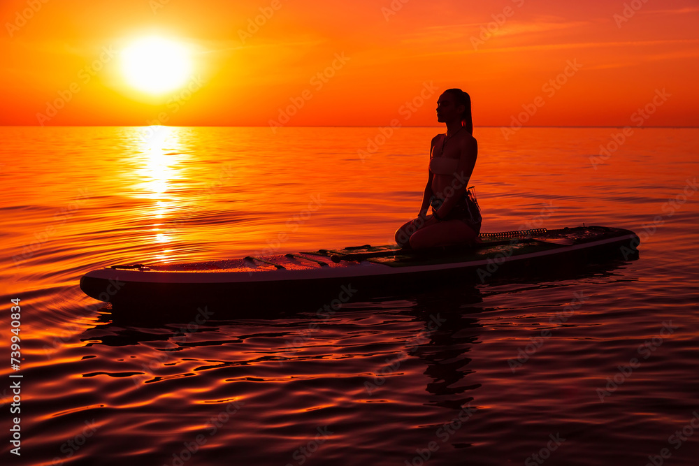 Silhouette of woman on paddle board at quiet sea with warm bright sunset or sunrise. Silhouette of woman on paddle board at quiet sea with warm bright sunset or sunrise.