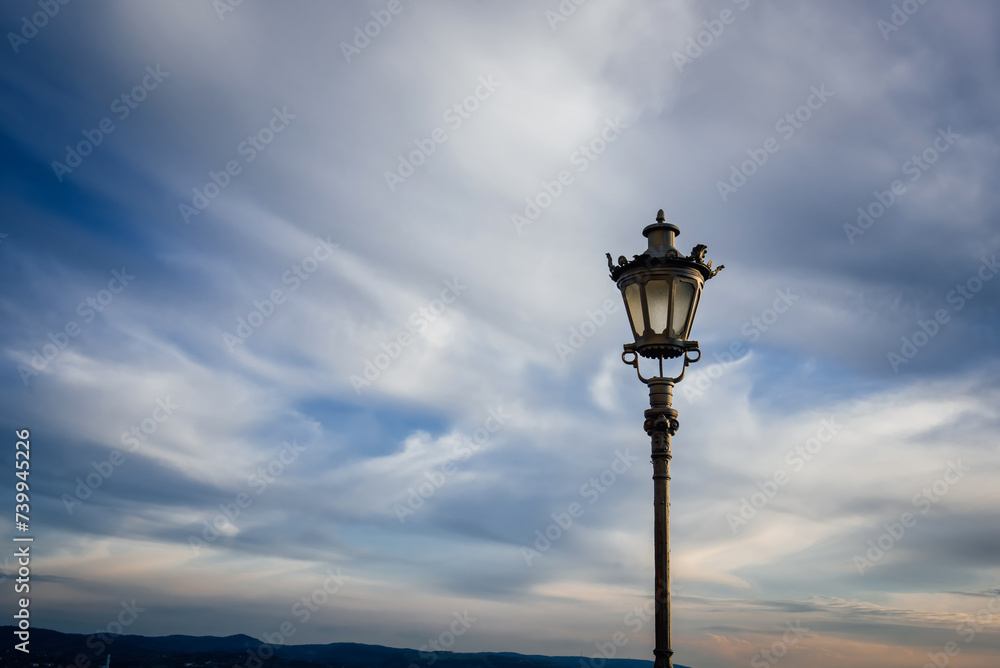 Historical lantern on the background of beautiful blue sky and clouds. Traditional vintage street lamp.