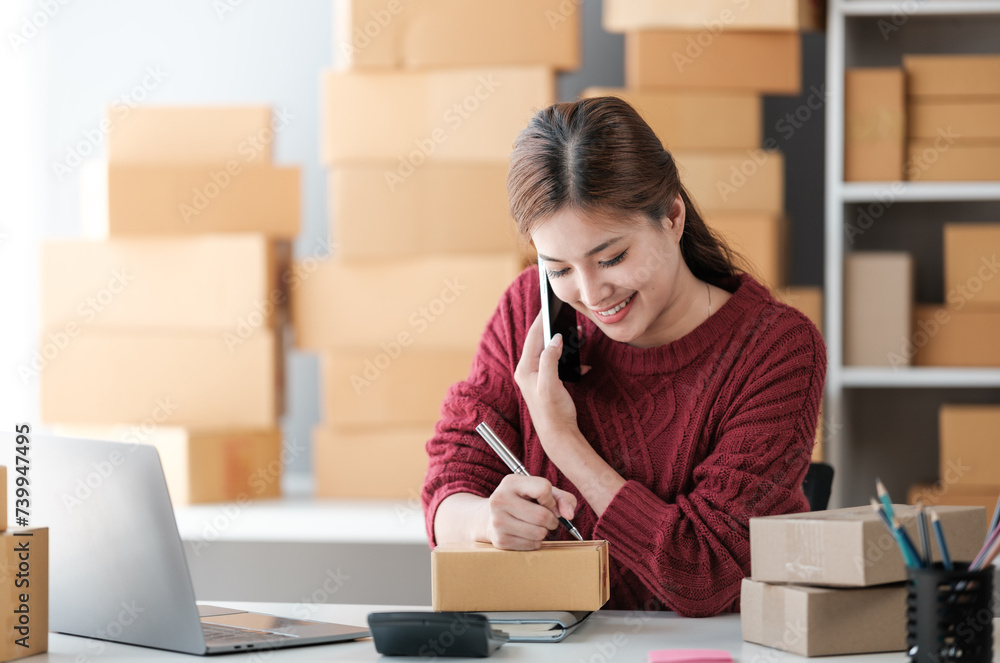 Startup SME small business entrepreneur of freelance Asian woman wearing apron using laptop and box to receive and review orders online to prepare to pack sell to customers, online sme business ideas. Startup SME small business entrepreneur of freelance Asian woman wearing apron using laptop and box to receive and review orders online to prepare to pack sell to customers, online sme business ideas.
