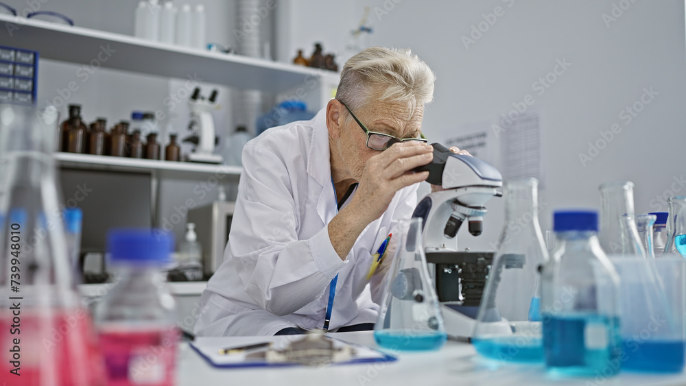 Dedicated grey-haired senior woman scientist immersed in intense microscope research work at phd level in lab Dedicated grey-haired senior woman scientist immersed in intense microscope research work at phd level in lab