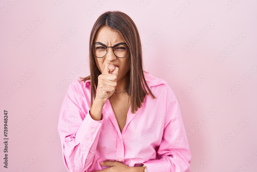 Young hispanic woman wearing glasses standing over pink background feeling unwell and coughing as symptom for cold or bronchitis. health care concept. Young hispanic woman wearing glasses standing over pink background feeling unwell and coughing as symptom for cold or bronchitis. health care concept.