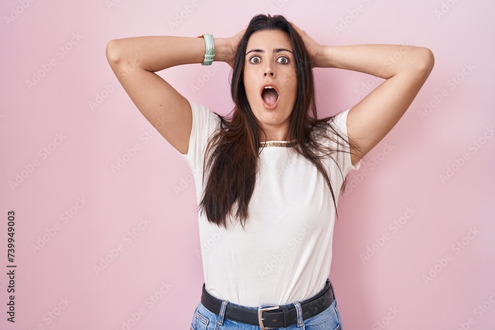 Young brunette woman standing over pink background crazy and scared with hands on head, afraid and surprised of shock with open mouth Young brunette woman standing over pink background crazy and scared with hands on head, afraid and surprised of shock with open mouth
