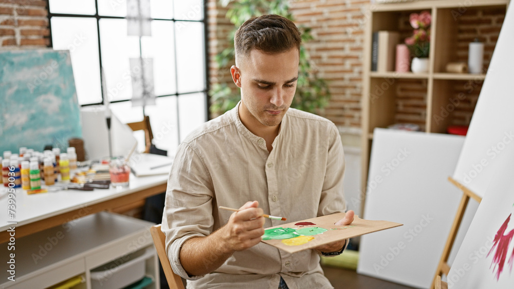 A young hispanic man focuses while painting on a canvas in an art studio environment, radiating creative and academic vibes.