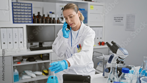Young blonde woman scientist talking on smartphone holding test tube at laboratory