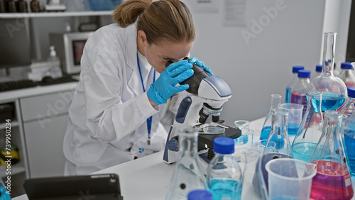 Attractive, focused blonde young woman scientist engrossed in her medical research using a microscope in lab, a portrait of determination working on scientific analysis