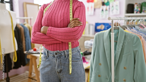 Confident black woman with folded arms wearing a measuring tape in a tailor shop.