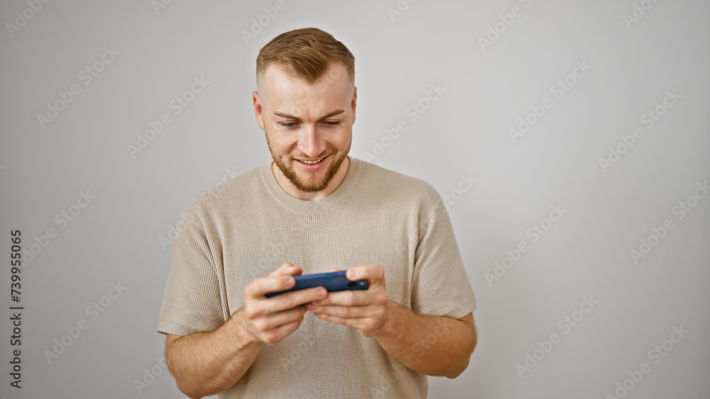 Handsome young adult caucasian man with beard smiling at smartphone in hand against isolated white background Handsome young adult caucasian man with beard smiling at smartphone in hand against isolated white background