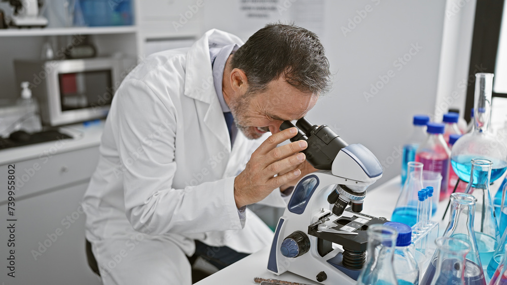 Aged man with grey hair, a scientist busy in his lab, peering into microscope for medical discovery Aged man with grey hair, a scientist busy in his lab, peering into microscope for medical discovery
