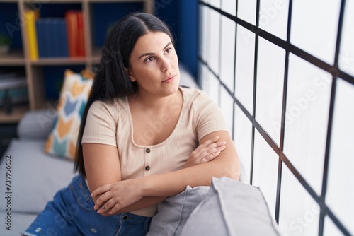 Young beautiful hispanic woman sitting on sofa with serious expression at home