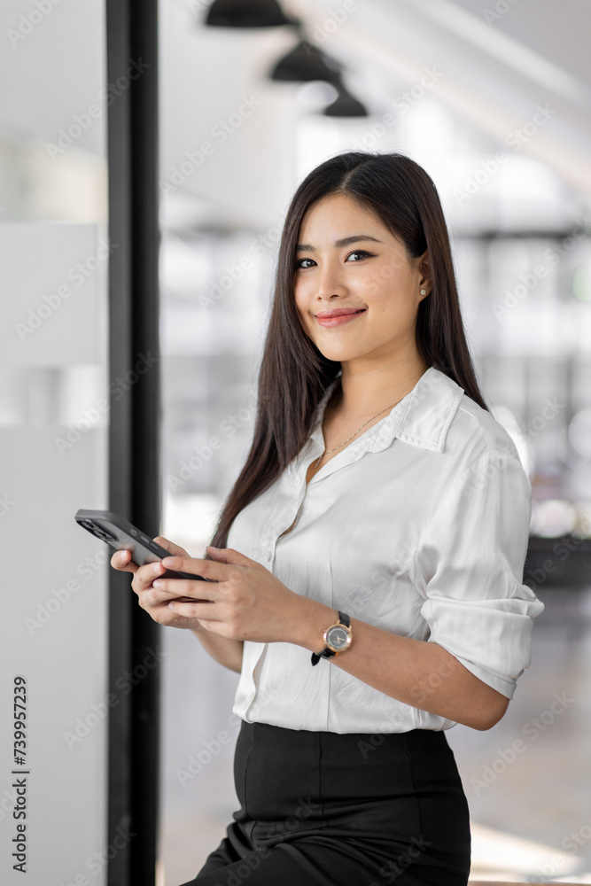 Smiling business asian woman using her phone in the office. Small business entrepreneur looking at her mobile phone and smiling while communicating with her office colleagues Smiling business asian woman using her phone in the office. Small business entrepreneur looking at her mobile phone and smiling while communicating with her office colleagues