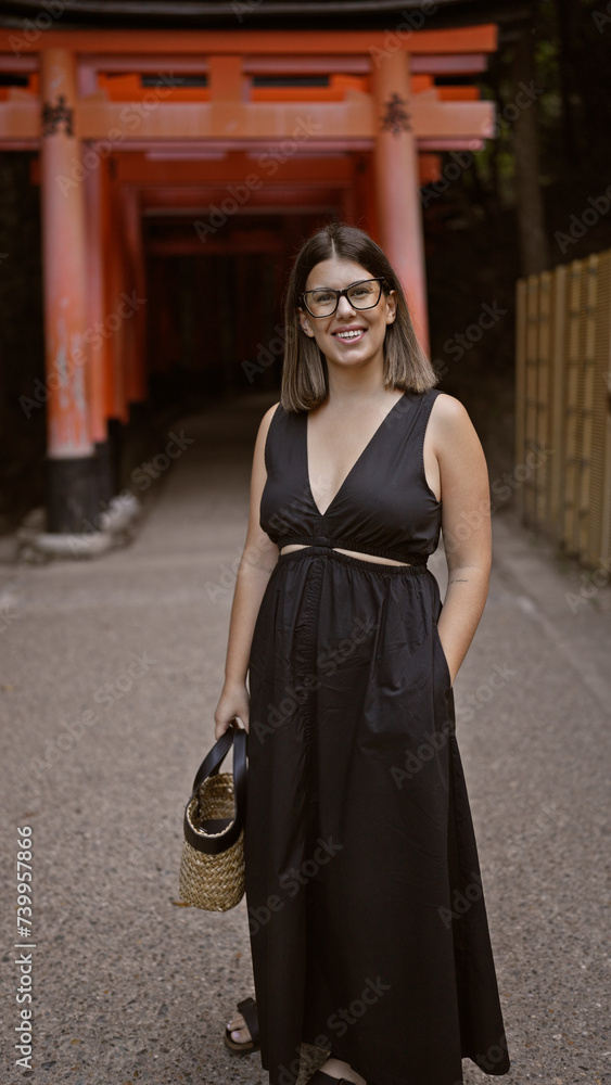 Gorgeous hispanic woman in glasses flaunting a radiant smile at the majestic torii gates of fushimi inari-taisha, kyoto