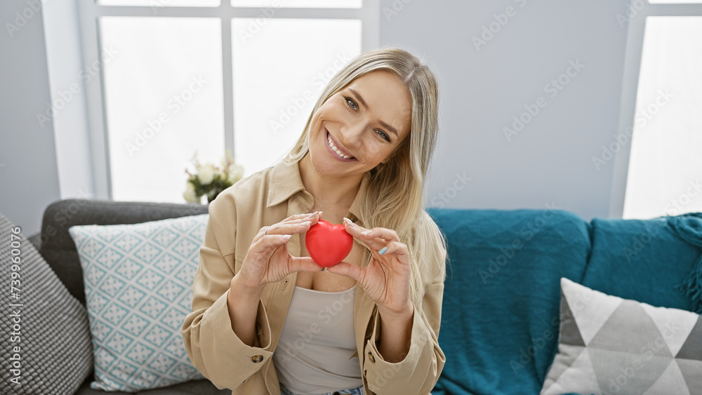 Young blonde woman holding heart sitting on sofa smiling at home Young blonde woman holding heart sitting on sofa smiling at home