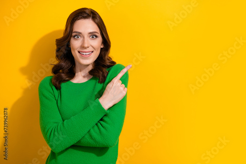 Photo of cheerful pretty girl wear green stylish pullover demonstrate profitable sale empty space isolated on yellow color background