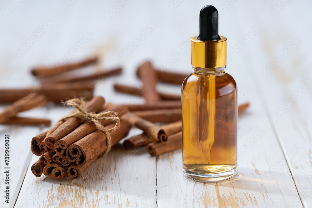 Cinnamon sticks and bottle of cinnamon oil on a white wooden table. Cinnamon sticks and bottle of cinnamon oil on a white wooden table.