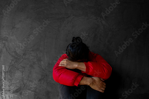 A man wearing a red  coat  sits with his head bent over and his knees hugged. A man feel very stressed. photo