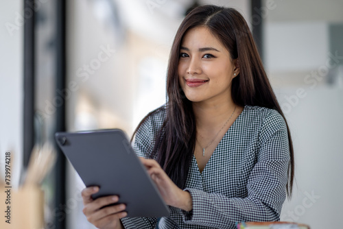 Young asian business woman executive, female company worker or manager holding digital tablet using technology device working standing in modern corporate office. © David
