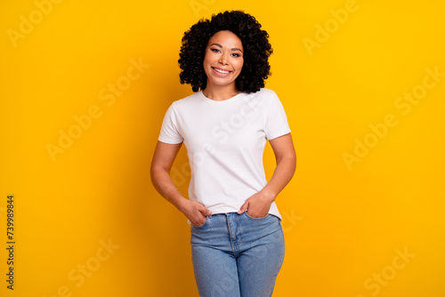 Photo of adorable cheerful woman with perming coiffure dressed white t-shirt keep arms in pockets isolated on yellow color background photo
