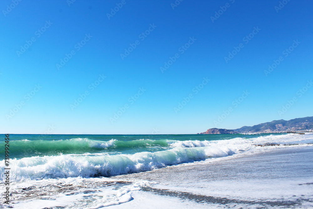 clear blue sky and waves with white foam at Mahmutlar beach in Turkey. mountains in the background