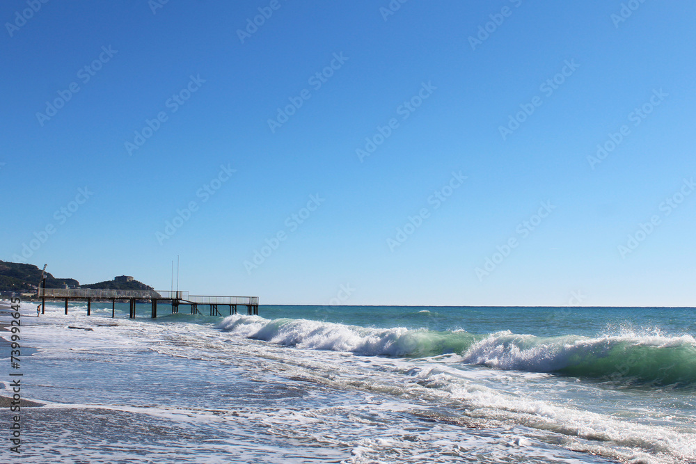 clear blue sky over the sea. big waves with white foam crashing on beach and sea pier in mediterranean sea