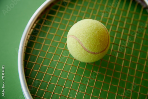 A yellow tennis ball lies on a tennis racket on a green background