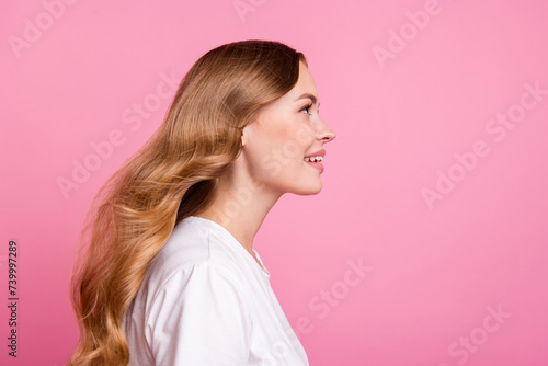 Side profile photo of gorgeous girl with fluttering hair dressed white t-shirt look at promo empty space isolated on pink color background