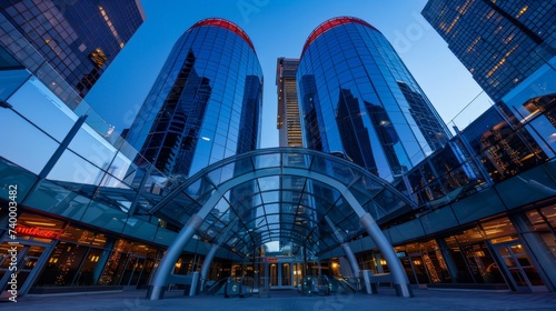 From below of entrance of office building next to contemporary high rise structures with glass mirrored walls and illuminated lights in calgary city against cloudless blue sky