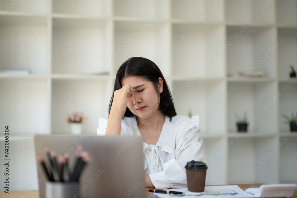 Young businesswoman stressed and having headache while working at desk with laptop in modern office Young businesswoman stressed and having headache while working at desk with laptop in modern office