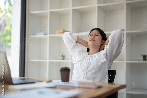 A female employee stretching lazy at the desk to relax while working in the office. Feeling stressed and achy from work. © Wasana