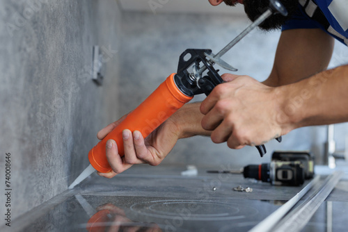 Worker seals up the kitchen countertop with a sealant using a construction sealing gun.