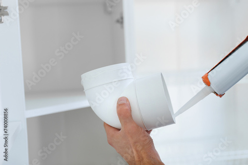 Man installs a hood and an air duct in kitchen, connects parts of the duct with sealant and glue.