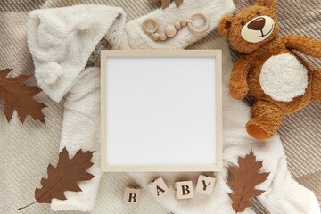 Pregnancy, baby coming announcement template, square wooden frame mockup, cozy fall flat lay composition with warm baby overalls, teddy bear toy, blanket, autumn leaves.