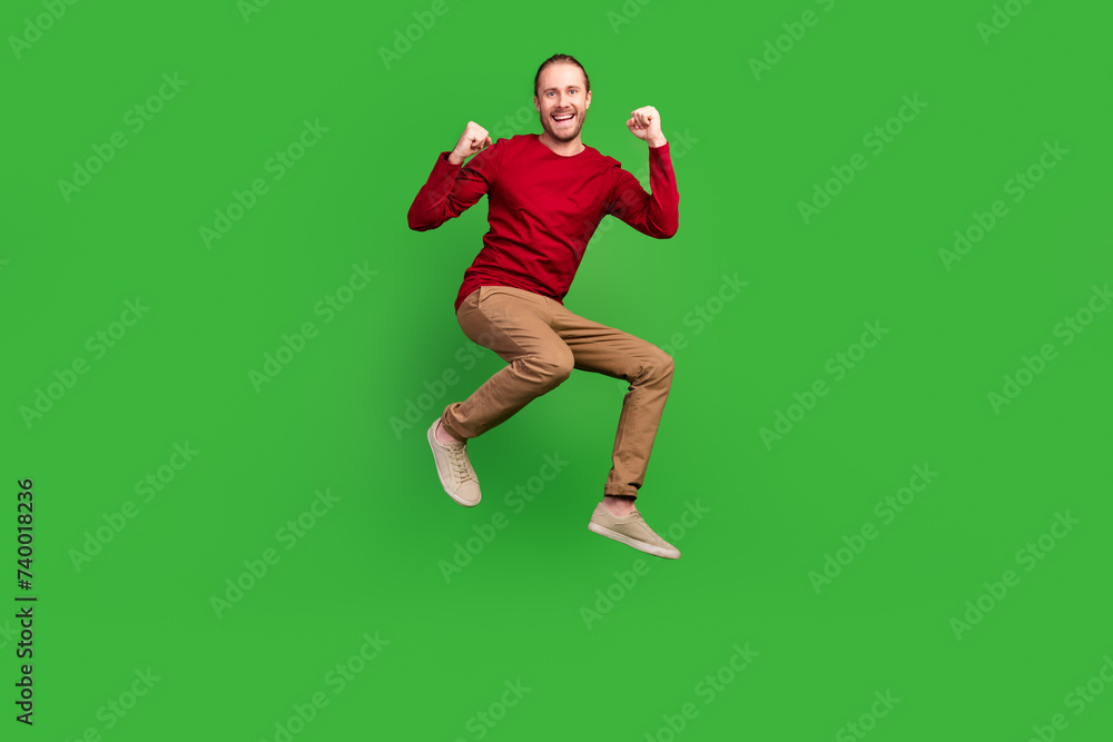 Full size photo of ecstatic man dressed red pullover brown pants jumping win gambling scream yeah isolated on green color background Full size photo of ecstatic man dressed red pullover brown pants jumping win gambling scream yeah isolated on green color background