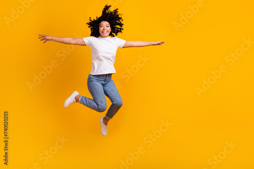 Full length photo of positive carefree woman wear white t-shirt jumping arms sides empty space isolated yellow color background