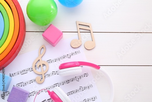 Notes, music sheet, headphones and toys on white wooden table, flat lay with space for text. Baby song concept