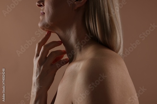 Woman touching her neck on beige background, closeup