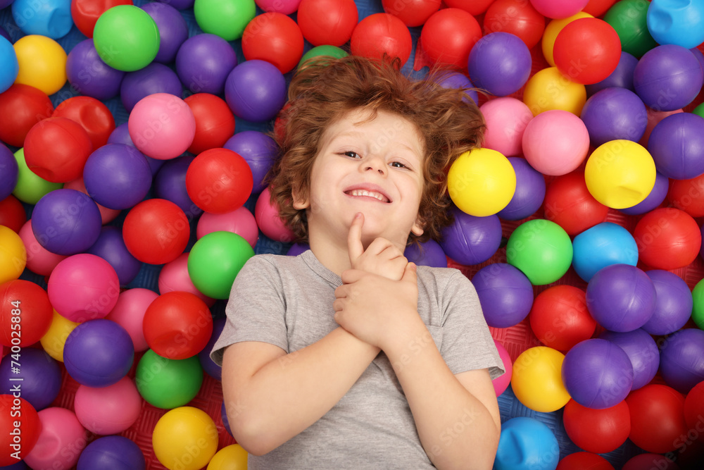 Obraz premium Happy little boy lying on many colorful balls, top view