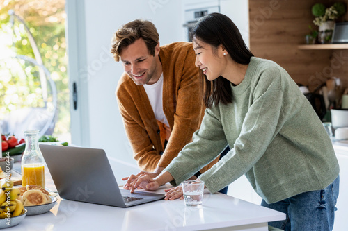 Adult couple using laptop together at kitchen counter