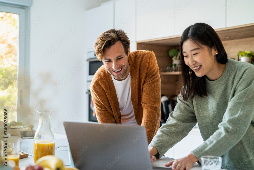 Adult couple shopping online on laptop while leaning on kitchen counter Adult couple shopping online on laptop while leaning on kitchen counter