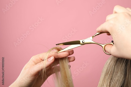 Hairdresser cutting client's hair with scissors on pink background, closeup. Space for text photo