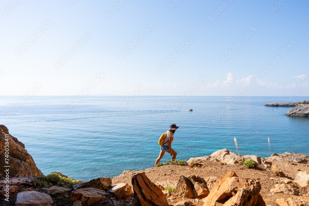 Woman with backpack enjoying a day of hiking by the sea in mountainous and semi-arid landscape on a Greek island on a late summer day