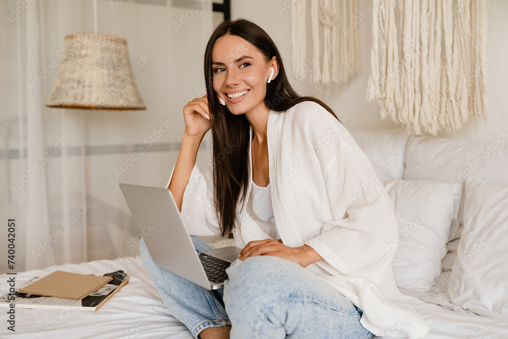 woman relaxing on bed at home in casual outfit using laptop listening to earpods woman relaxing on bed at home in casual outfit using laptop listening to earpods
