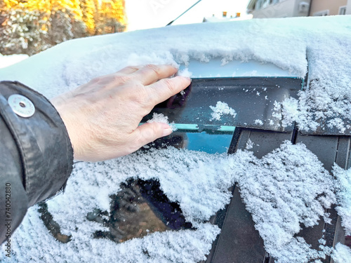 Hand of Woman persons brushing snow of a car window, which frozen over during a bitterly cold morning. Problem with travel and trip in winter photo