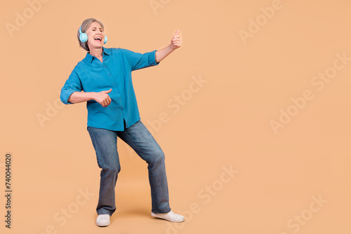 Full size photo of funky crazy retired woman dressed stylish shirt in headphones play imaginary guitar isolated on pastel color background