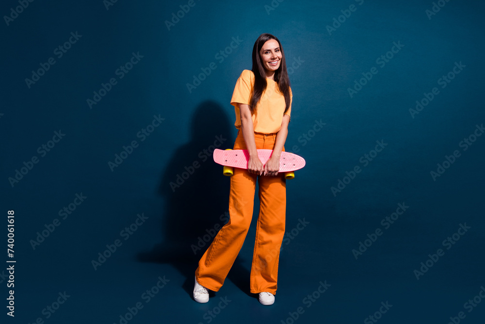 Full body size photo of beautiful smiling female rider skateboard satisfied posing model shy isolated over dark blue color background Full body size photo of beautiful smiling female rider skateboard satisfied posing model shy isolated over dark blue color background